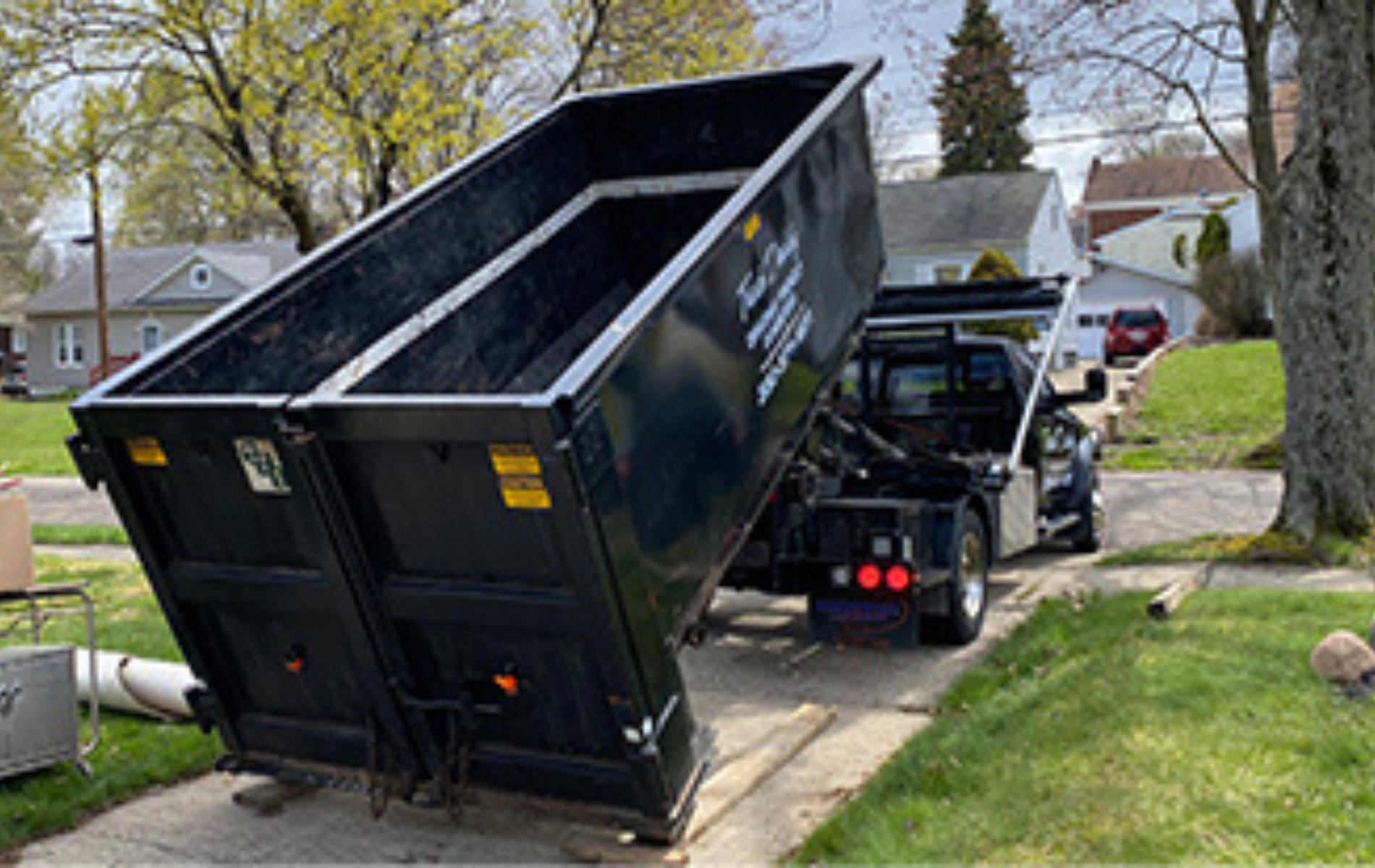 A dumpster is sitting on the side of a road next to a truck.