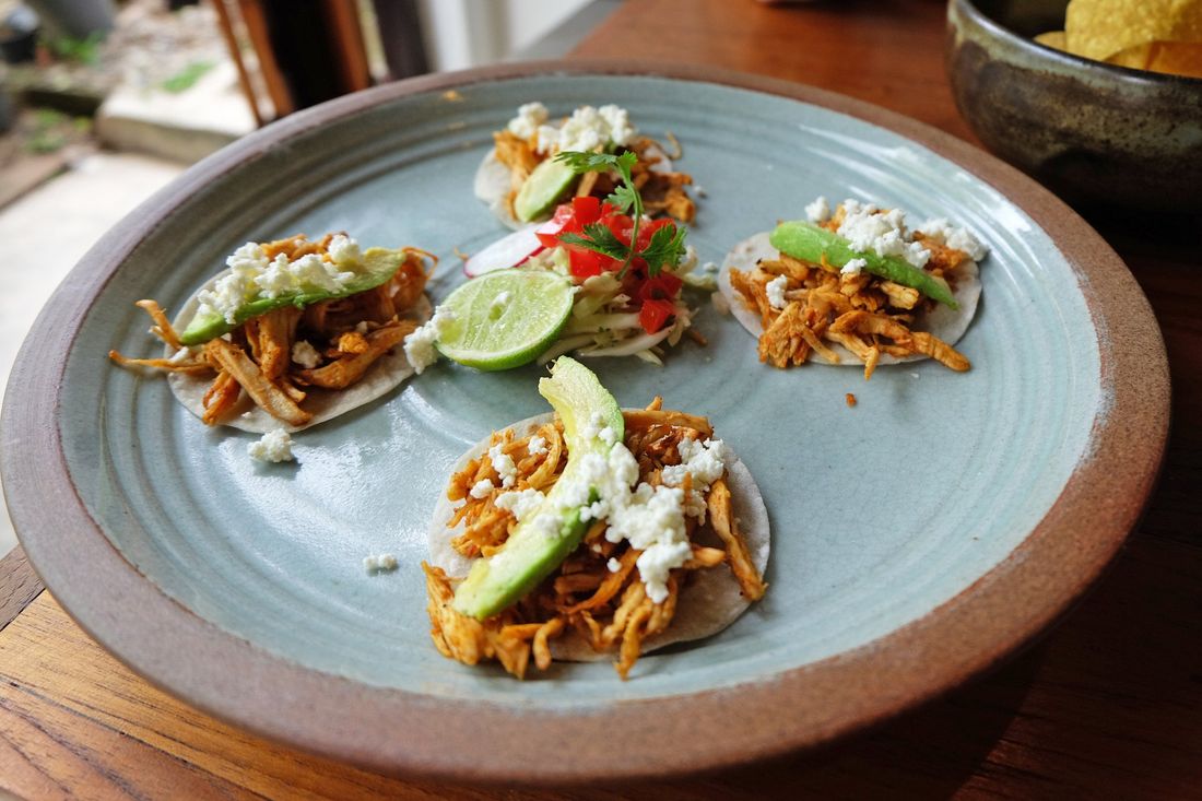 A plate of tacos with avocado and cheese on a wooden table.