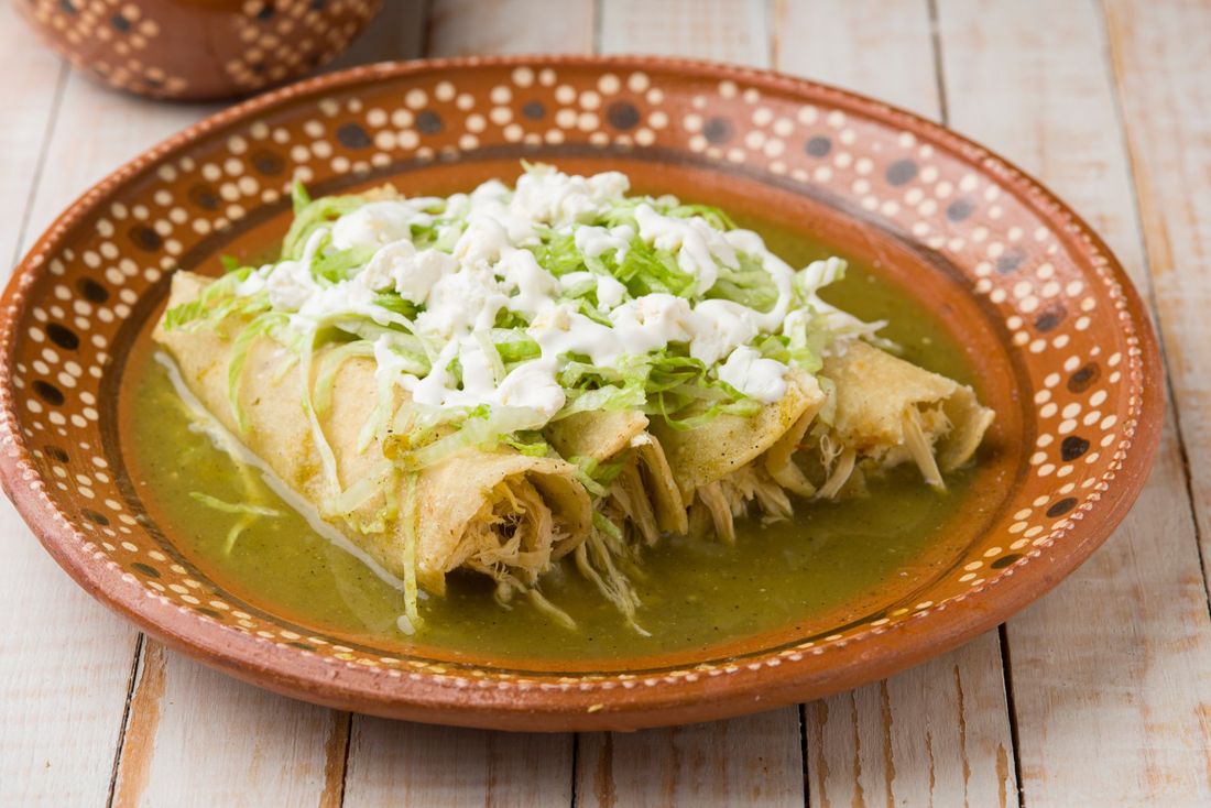 A plate of enchiladas with green sauce and cheese on a wooden table.