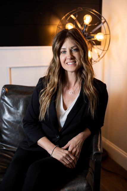 a woman in a black suit is sitting in a chair .