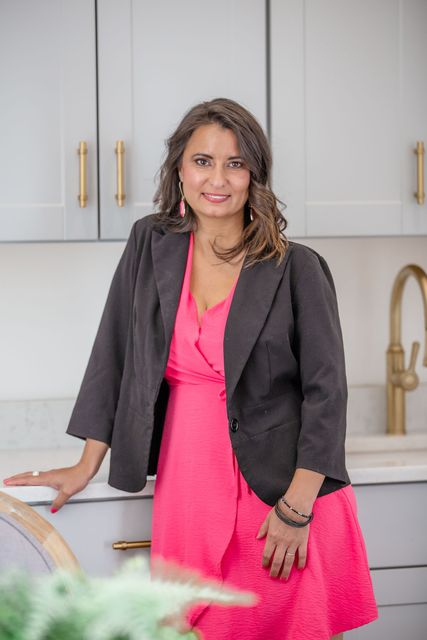 a woman in a pink dress and a black jacket is standing in a kitchen .