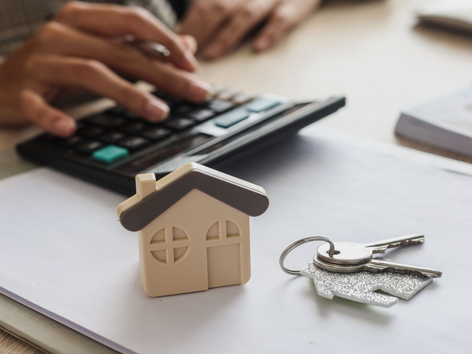 a person is using a calculator next to a model house and keys .