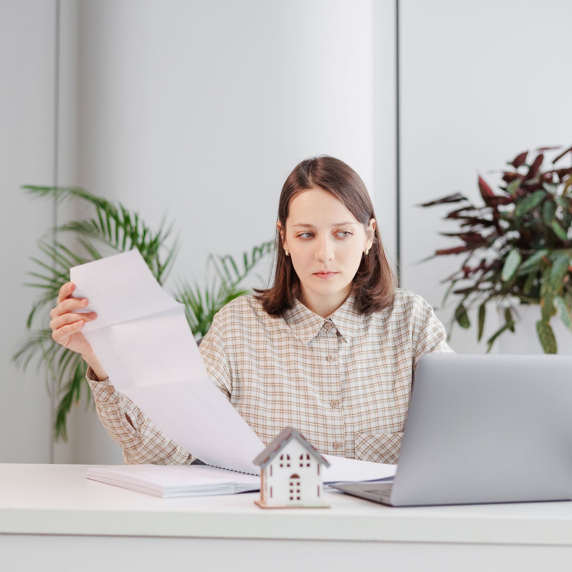 a woman is sitting at a desk with a laptop and holding a piece of paper .