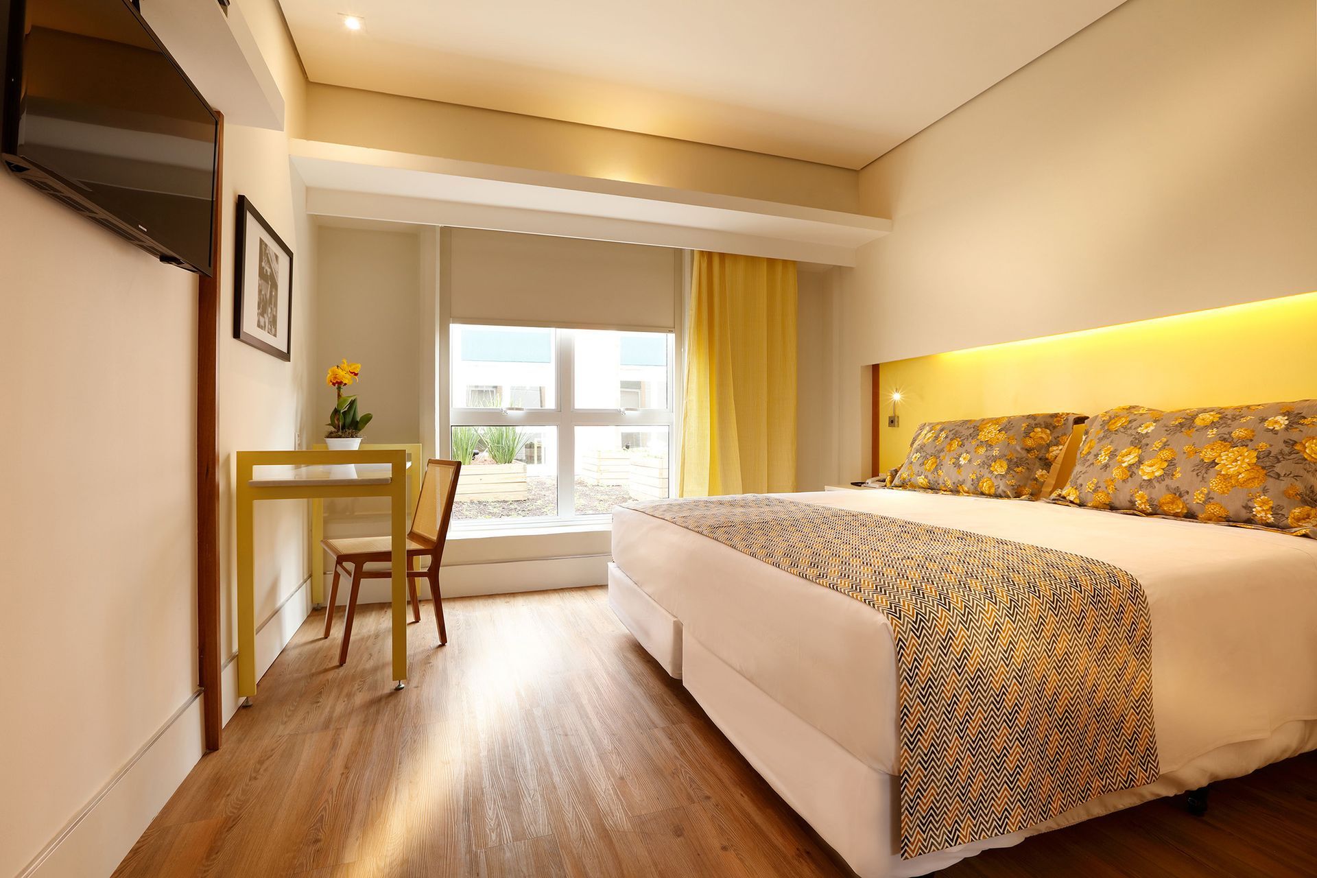 Um quarto de hotel com uma cama king size, escrivaninha, cadeira e televisão.