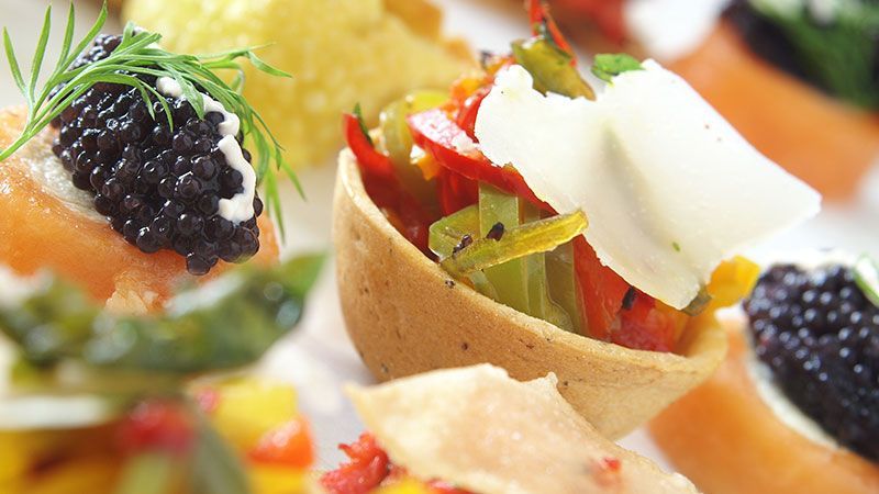 Close-up de aperitivos gourmet em cestinhas de massa folhada, cobertos com caviar preto e ervas.