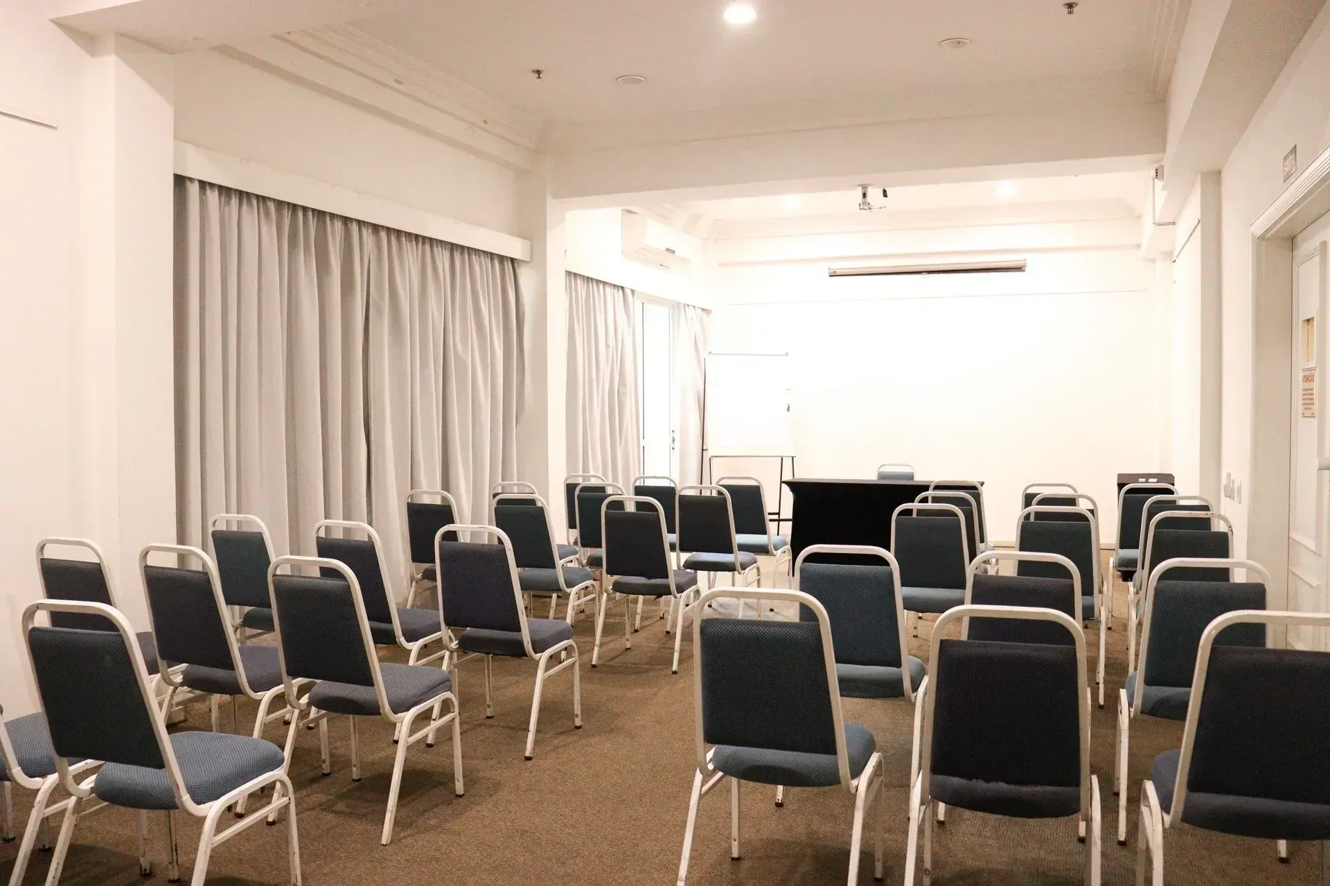 Sala de conferências vazia com fileiras de cadeiras azuis e um pódio na frente.
