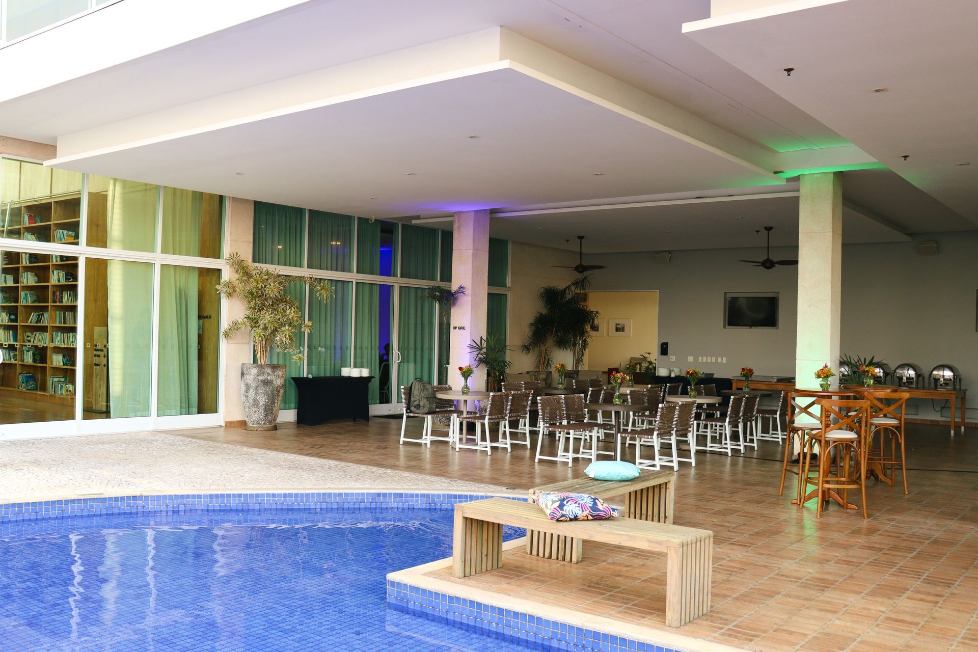 Pátio interno junto à piscina com espreguiçadeiras e mesas de jantar sob um terraço coberto.