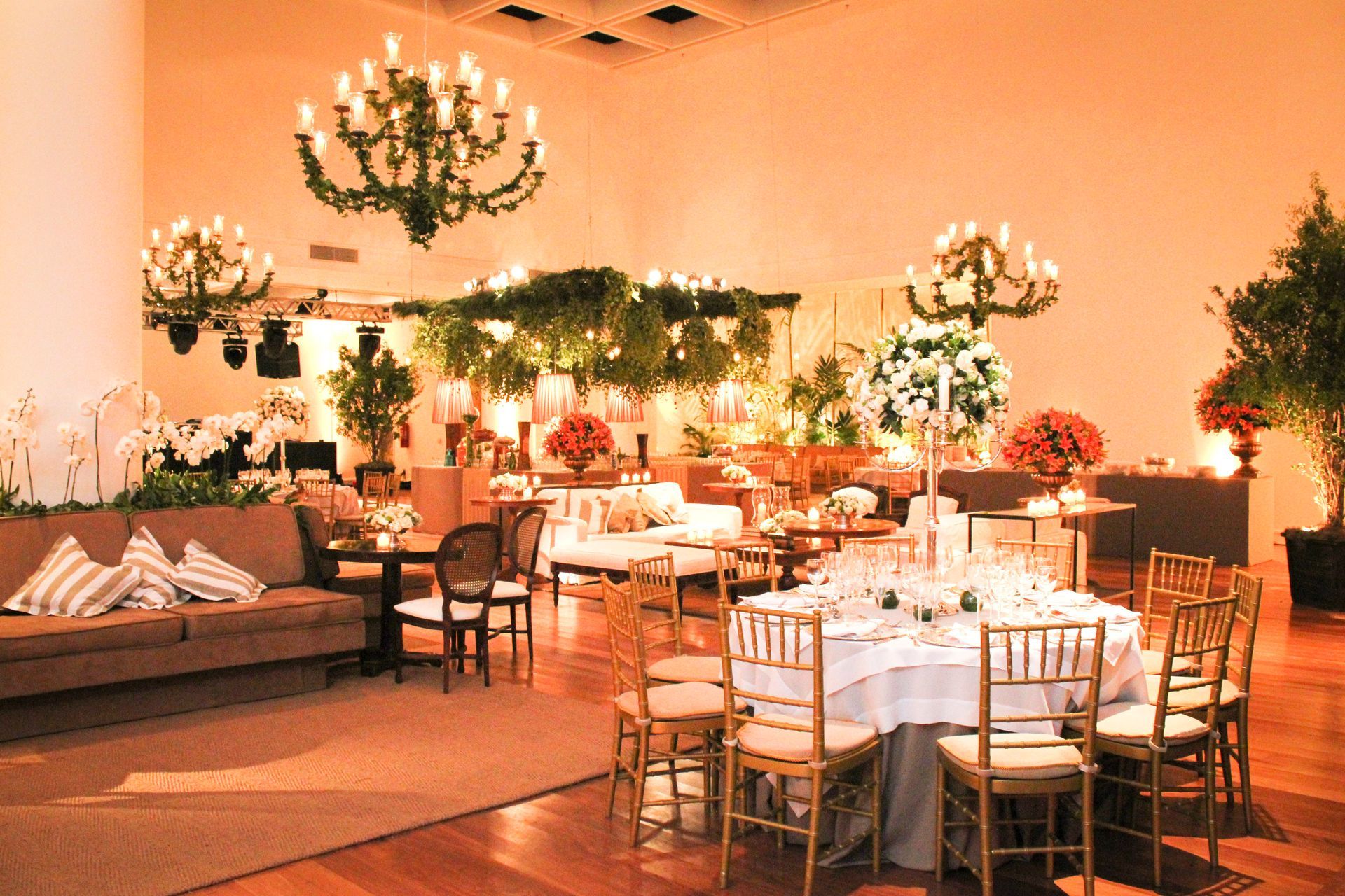Salão de banquetes elegante com mesas redondas, lustres e iluminação aconchegante em tons de laranja.