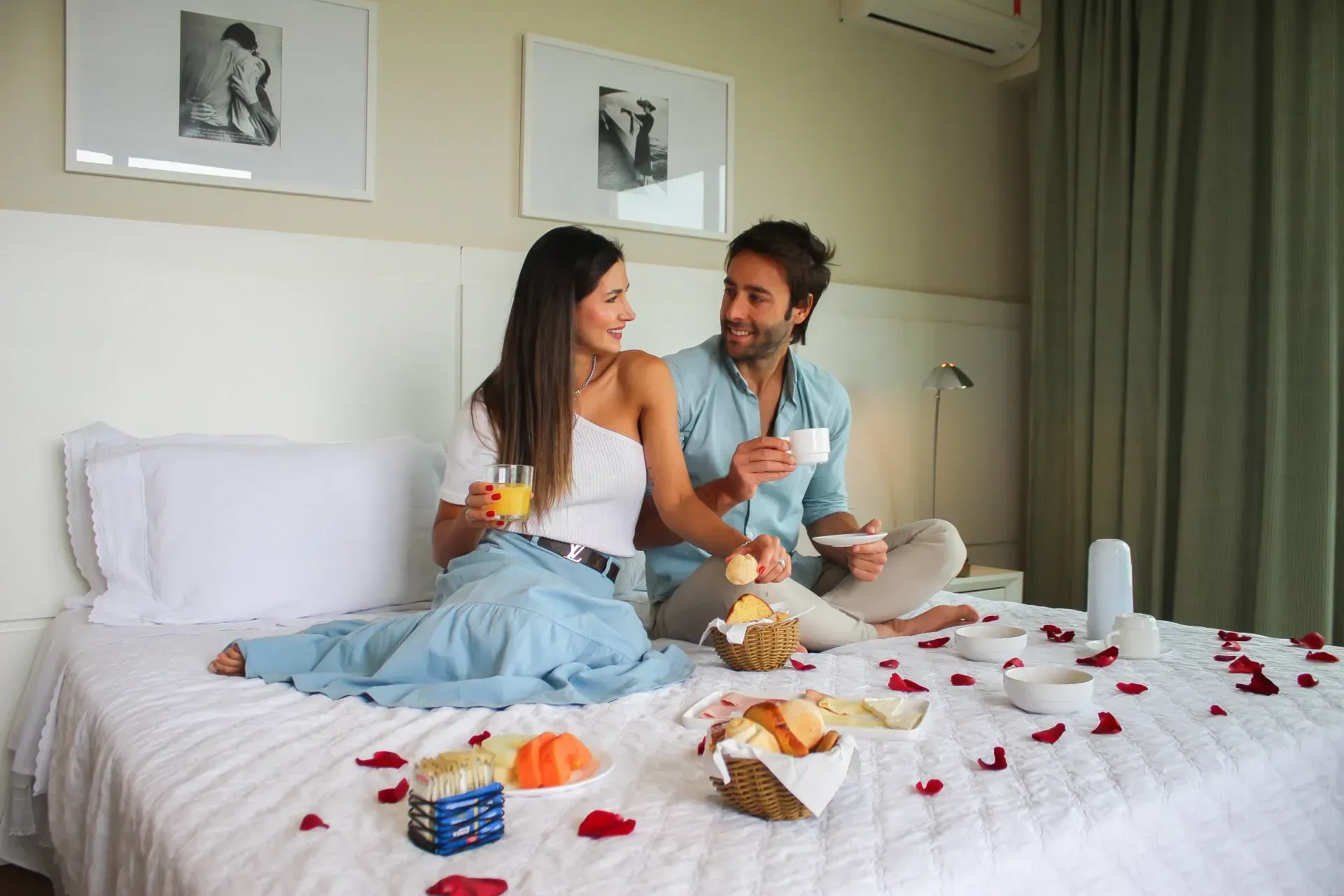 Um homem e uma mulher estão sentados em uma cama com itens de café da manhã espalhados na cama