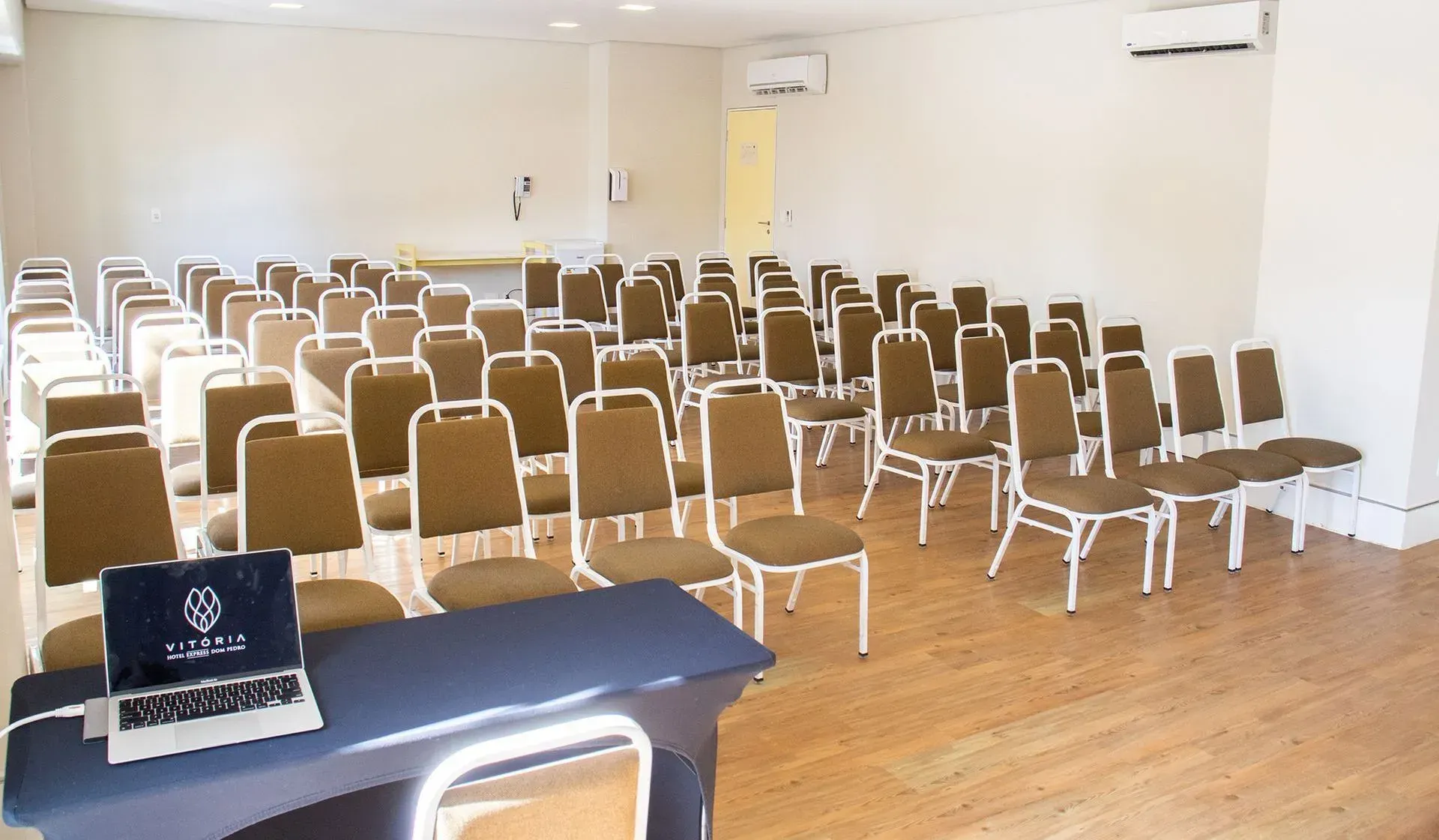 Uma sala de conferências com fileiras de cadeiras e um laptop sobre uma mesa.