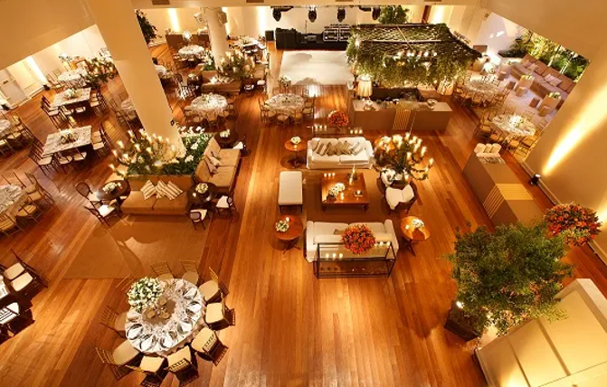 Sala de jantar elegante de restaurante com piso de madeira, mesas redondas e iluminação ambiente aconchegante, com vista panorâmica do alto.