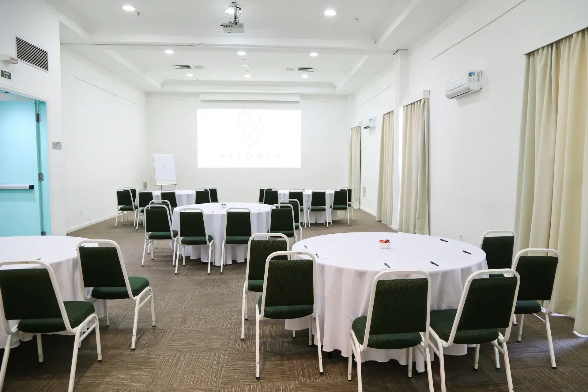 Uma sala grande com mesas e cadeiras e uma tela de projetor.