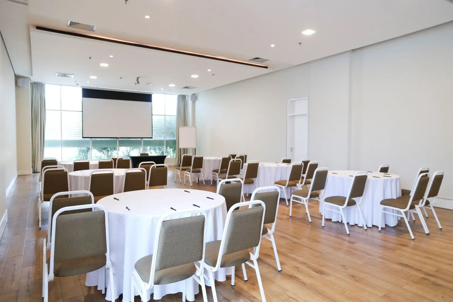 Uma sala grande com mesas e cadeiras e uma tela de projetor.