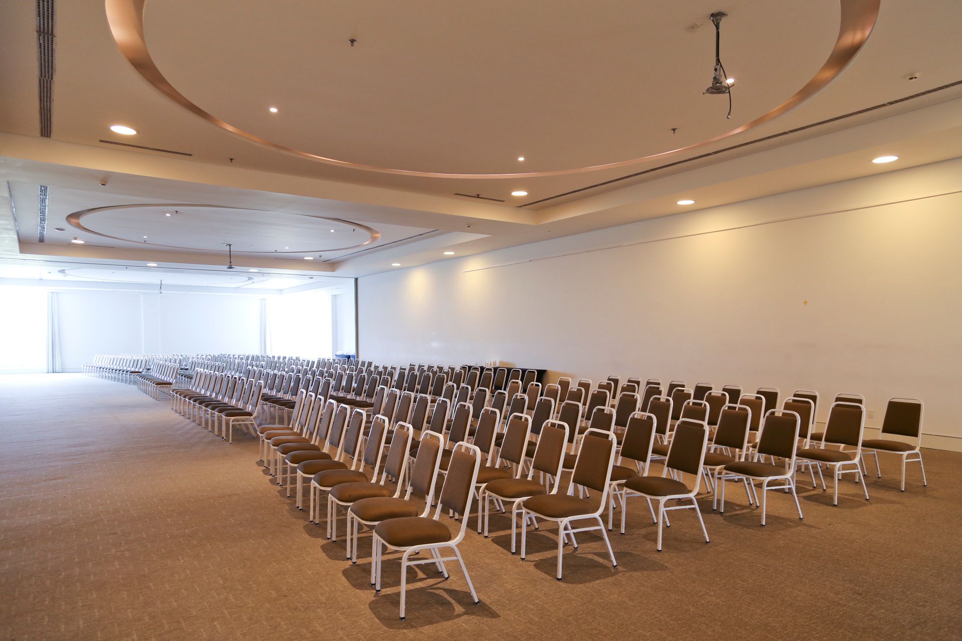 Sala de conferências vazia com fileiras de cadeiras voltadas para um palco iluminado ou área com tela.