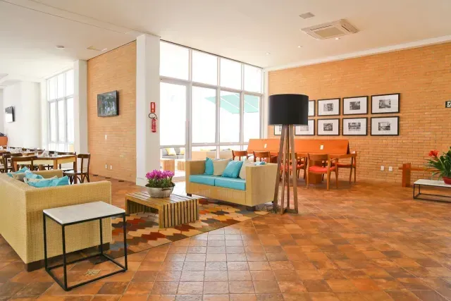 Sala de estar moderna com sofás turquesa, cadeiras de jantar laranja, janelas amplas e obras de arte emolduradas na parede.