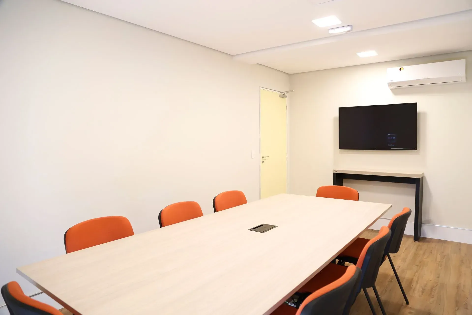 Uma sala de conferências com uma mesa longa, cadeiras e uma TV de tela plana.