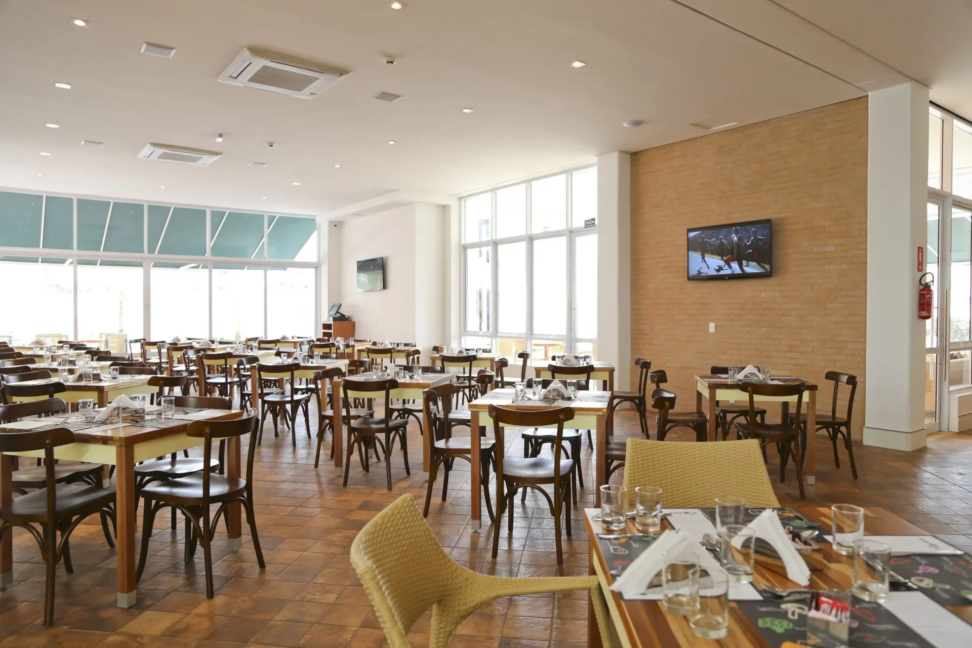 Sala de jantar ampla e iluminada do restaurante, com mesas e cadeiras de madeira e grandes janelas.