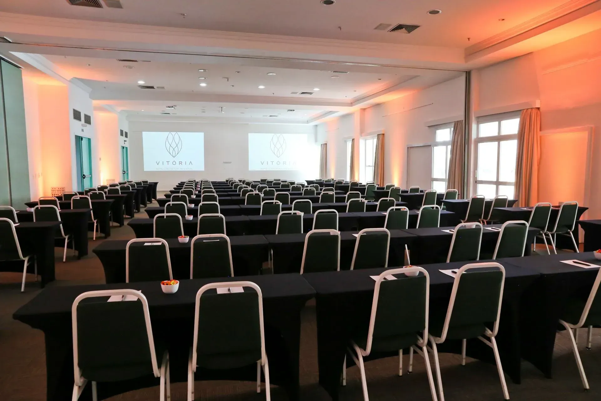 Uma grande sala de conferências com mesas e cadeiras e uma tela de projetor.