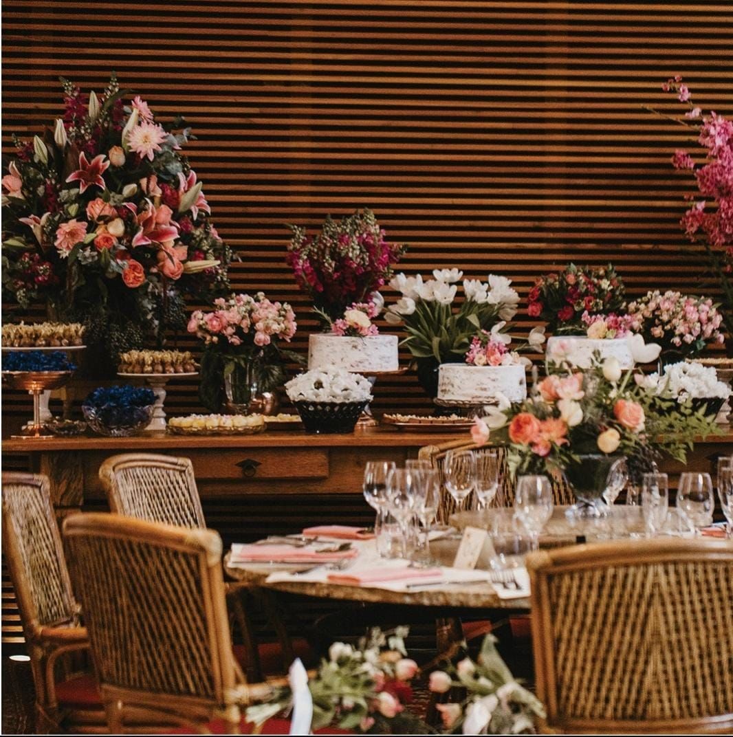 Mesa de banquete repleta de flores, com cadeiras de vime e taças de cristal, em um restaurante com iluminação aconchegante.
