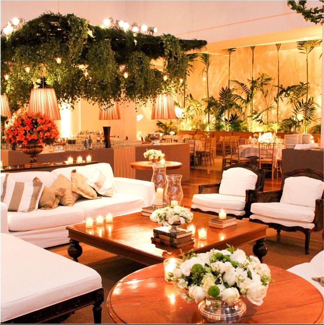 Sala de estar elegante com sofás brancos, mesas de madeira, arranjos florais e luzes de cordão aconchegantes sob folhagens.