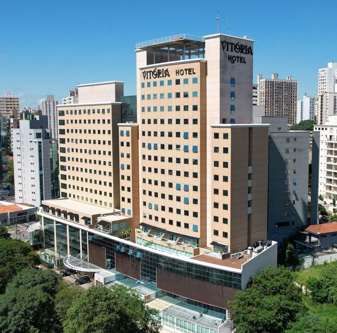 Alto prédio de hotel bege com sinalização no telhado, em meio à paisagem urbana.