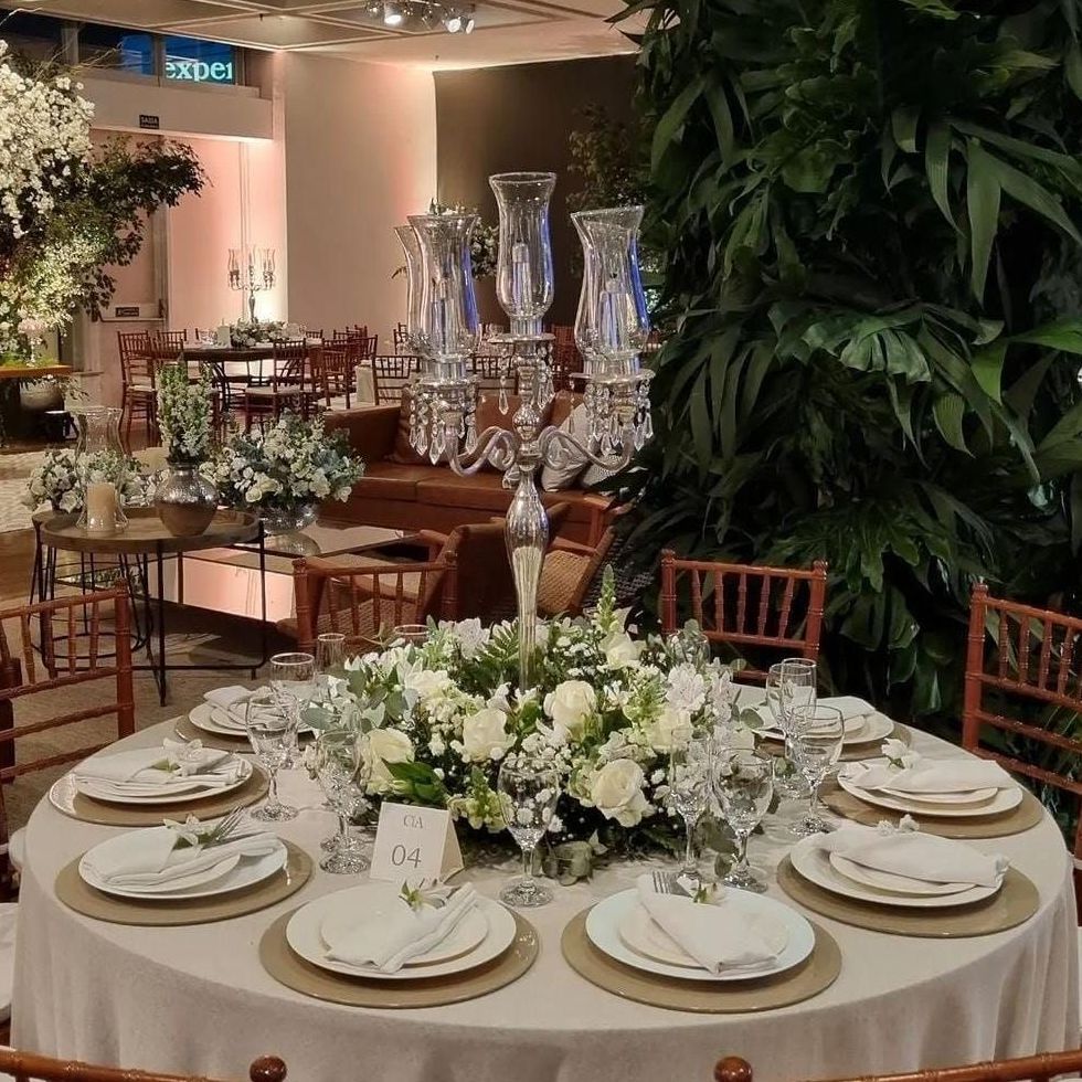 Elegante mesa de banquete com arranjo floral branco no centro e lugares marcados em um exuberante espaço para eventos interno.
