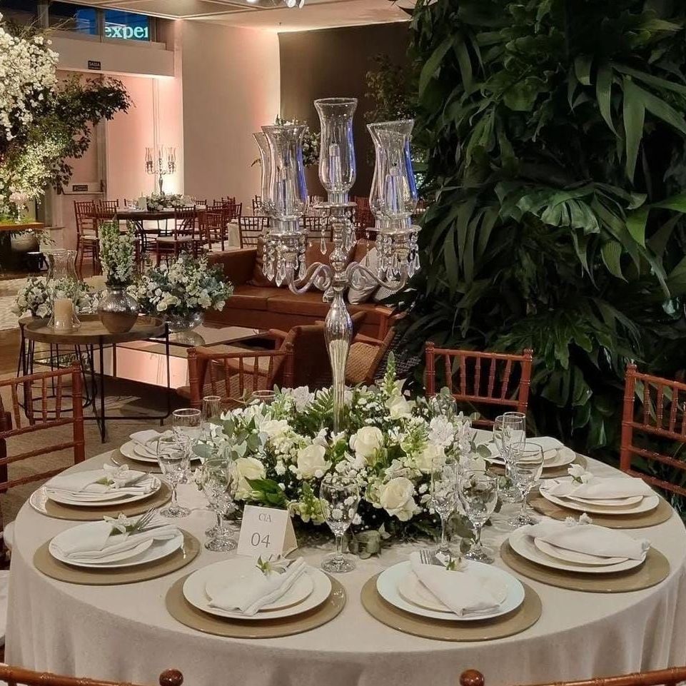 Elegante mesa de banquete com arranjo floral branco no centro e lugares marcados em um salão de eventos com iluminação aconchegante.