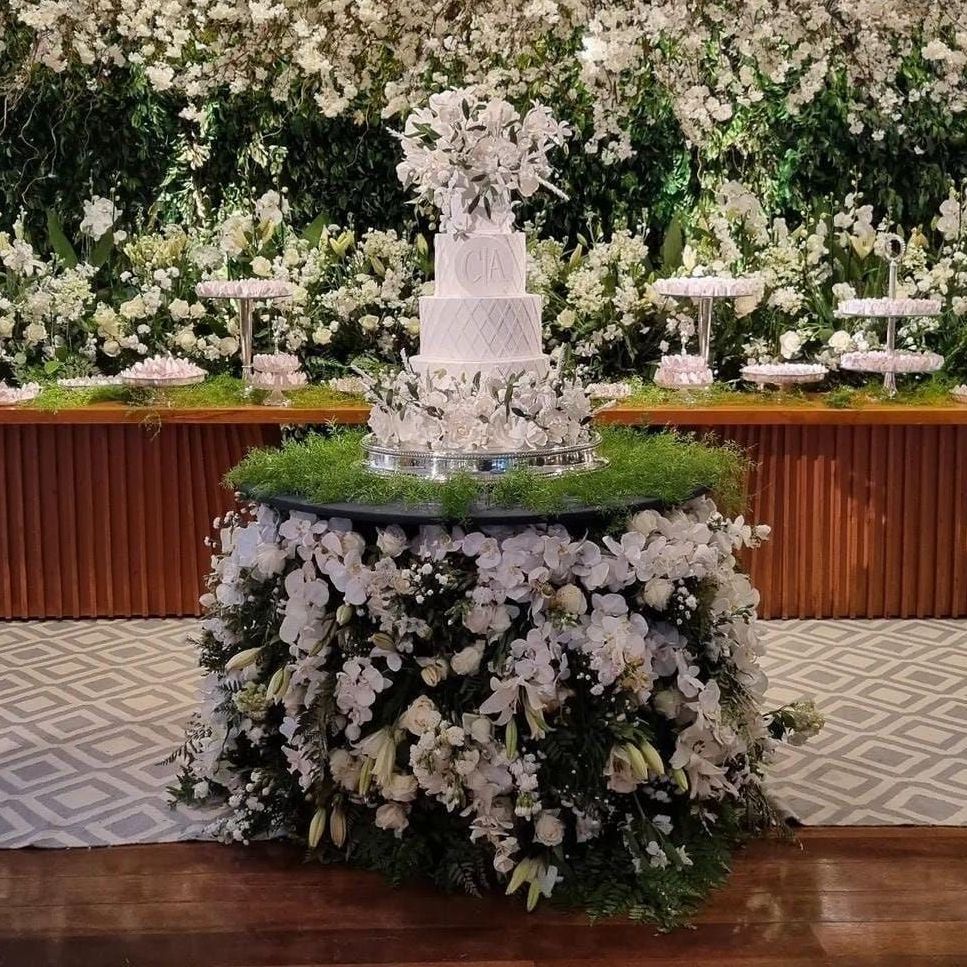 Elegante arranjo de mesa com fonte floral branca sobre uma mesa de madeira em um local decorado para eventos.