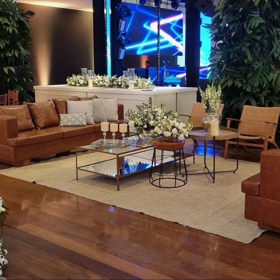 Sala de estar elegante com sofás de couro, mesa de centro de vidro, flores brancas e palco com iluminação azul.
