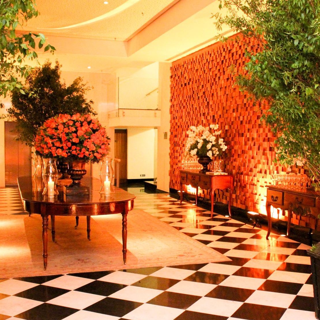 Hall de entrada elegante com piso xadrez preto e branco, arranjos florais e iluminação aconchegante em tons de laranja.
