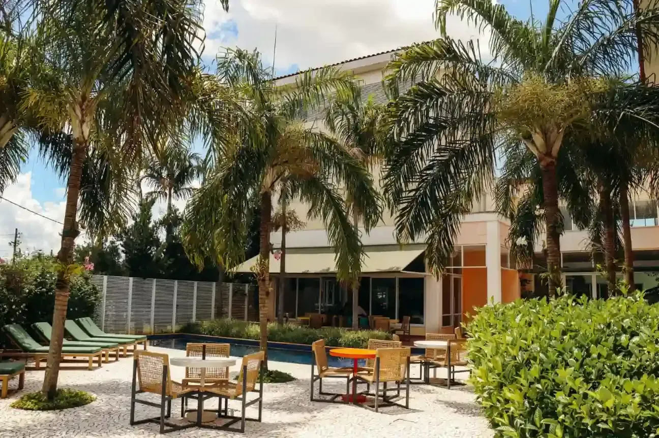 Pátio externo com palmeiras, espreguiçadeiras e mesas em frente a um prédio moderno.