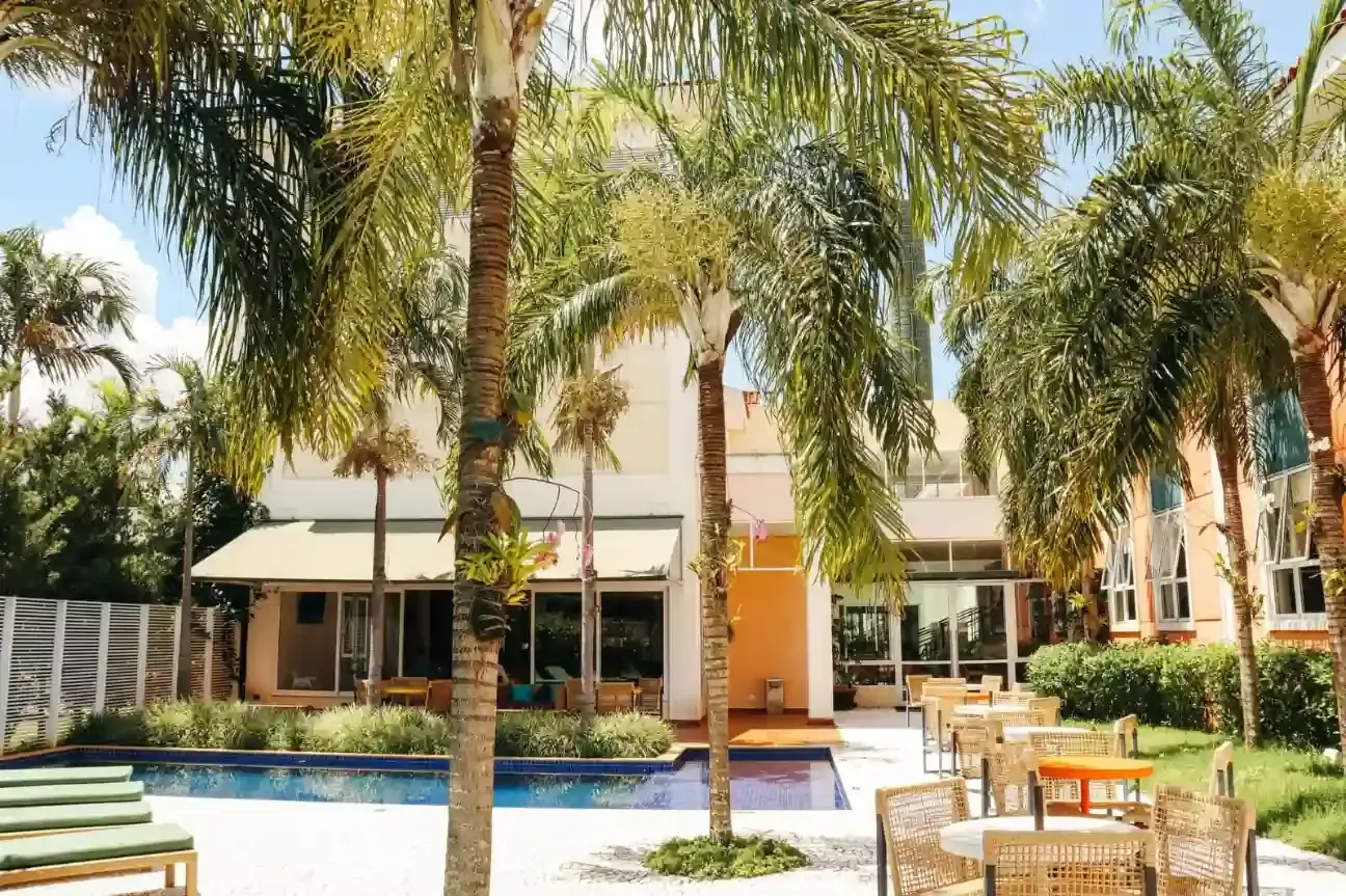 Piscina de resort rodeada por palmeiras, com espreguiçadeiras e um edifício moderno ao fundo.