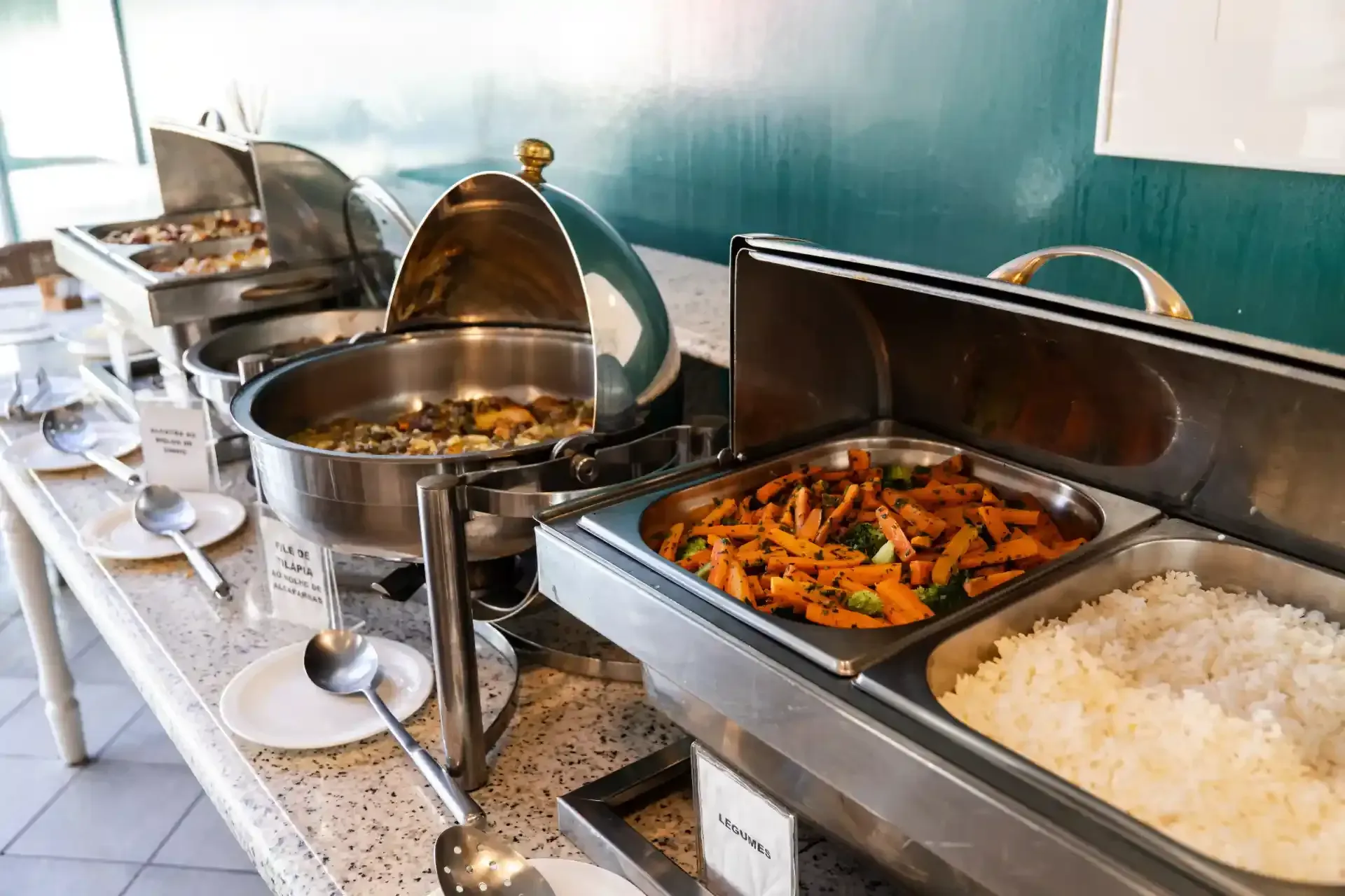 Balcão de buffet com bandejas cobertas contendo arroz, legumes e molhos.