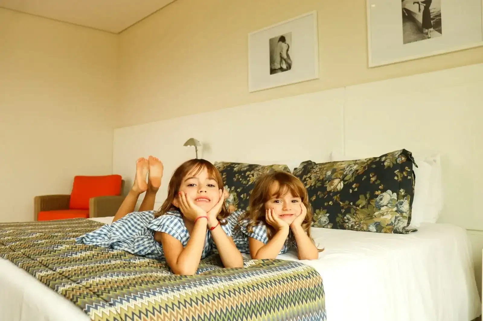 Duas crianças deitadas em uma cama, sorrindo em um quarto iluminado.