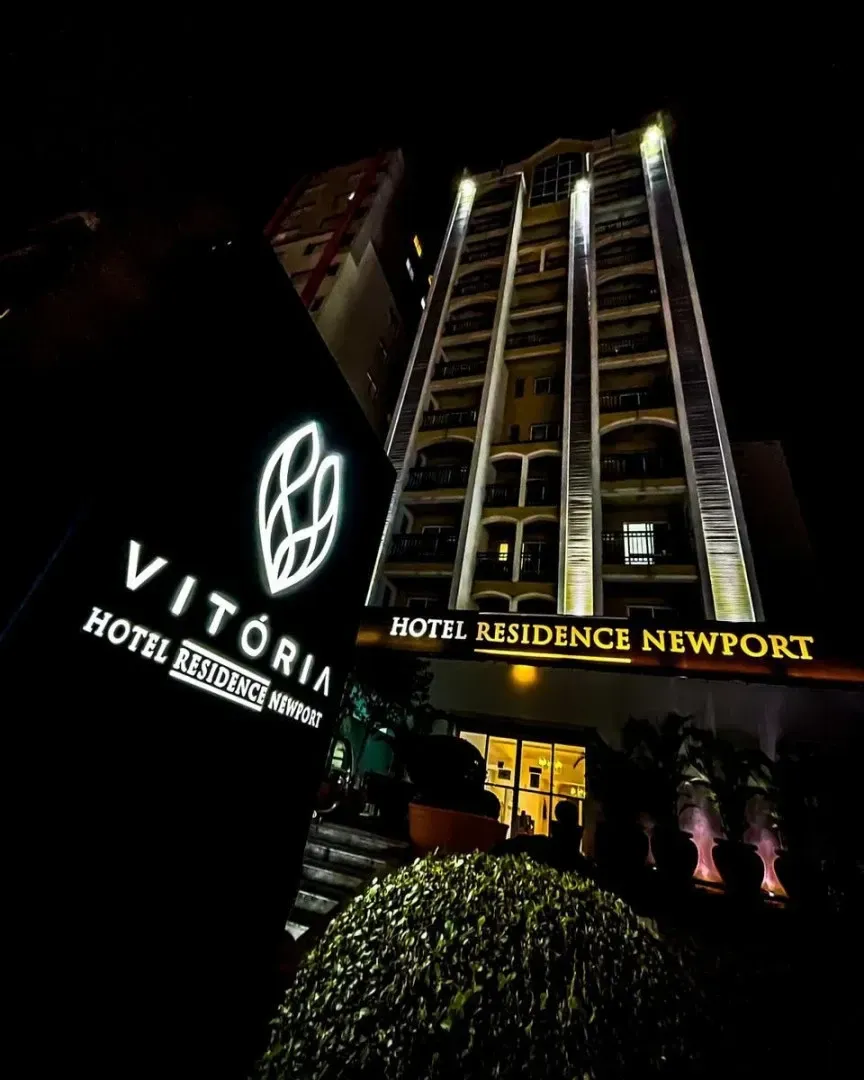 Vista noturna da entrada do Vitoria Hotel Residence Newport com fachada e sinalização iluminadas.