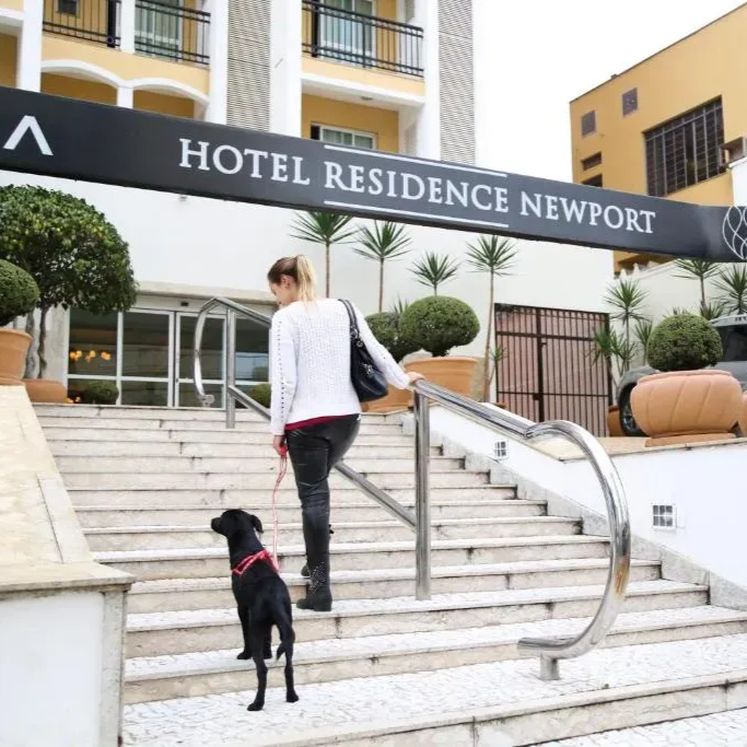 Mulher com cachorro preto na escadaria da entrada do Hotel Residence Newport