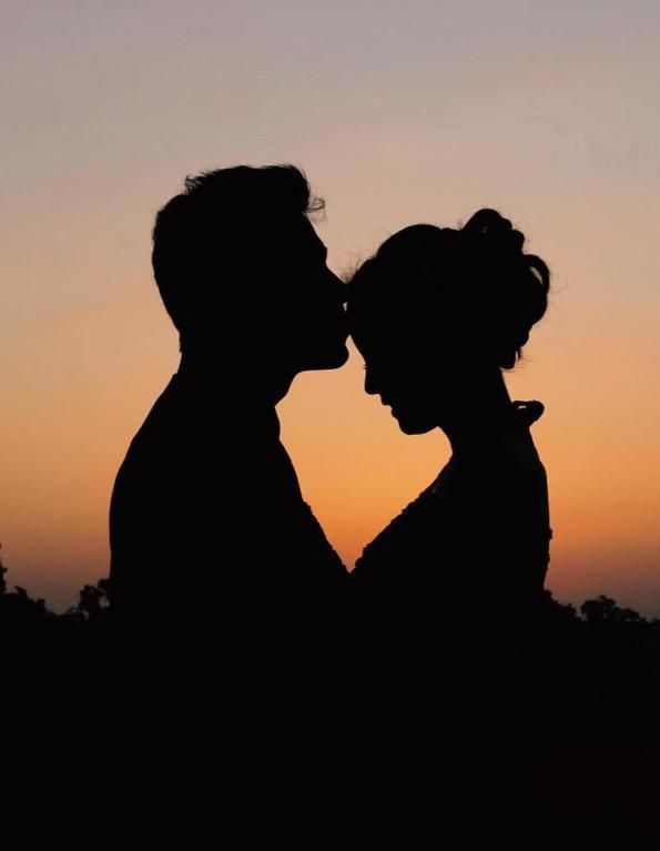 Silhueta de um casal encostando as testas ao pôr do sol, com um céu rosa-alaranjado.