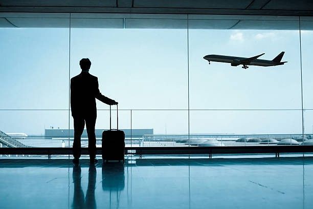 homem com mala de rodinha olhando avião decolar