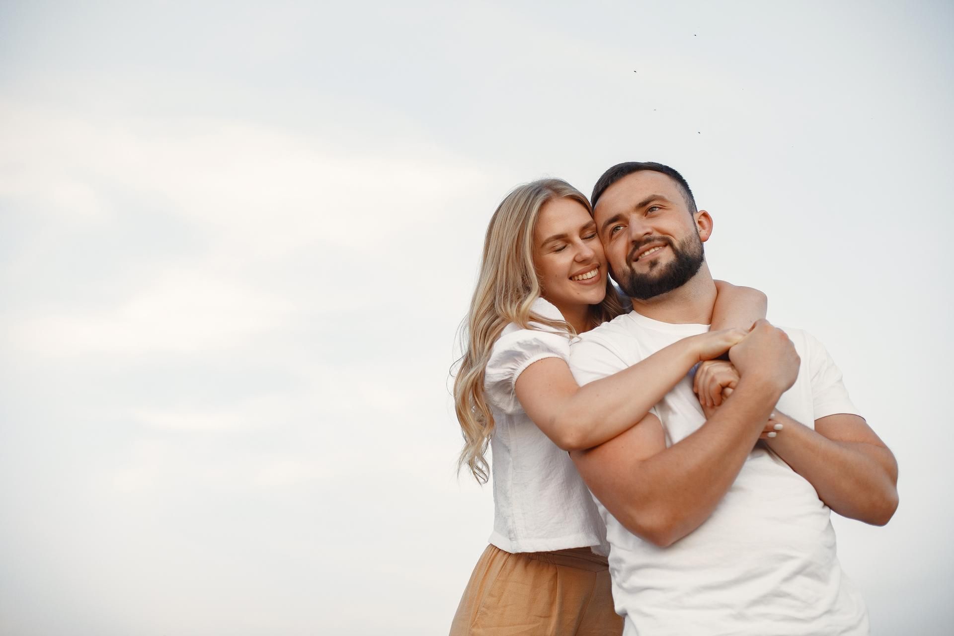 Casal sorridente se abraçando ao ar livre contra um céu claro.
