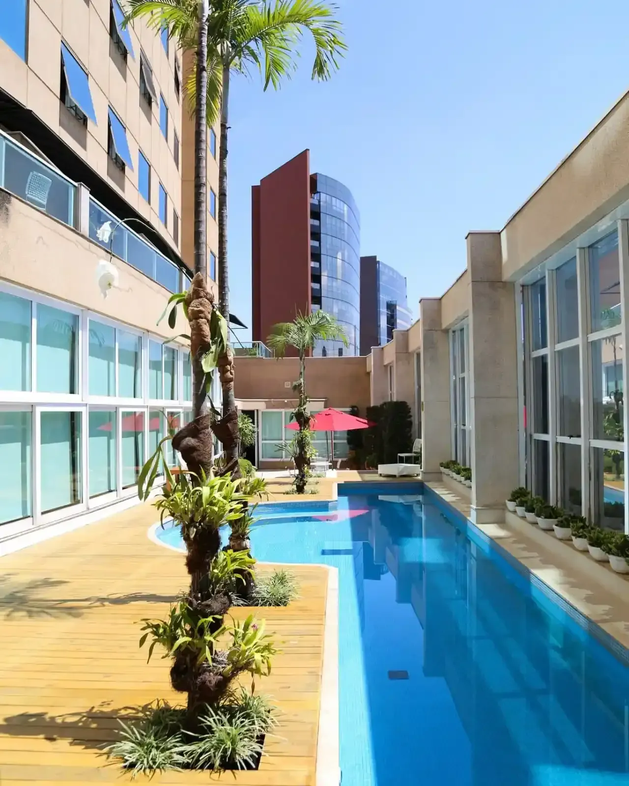 Pátio junto à piscina com piscina azul, deck de madeira e edifícios modernos.