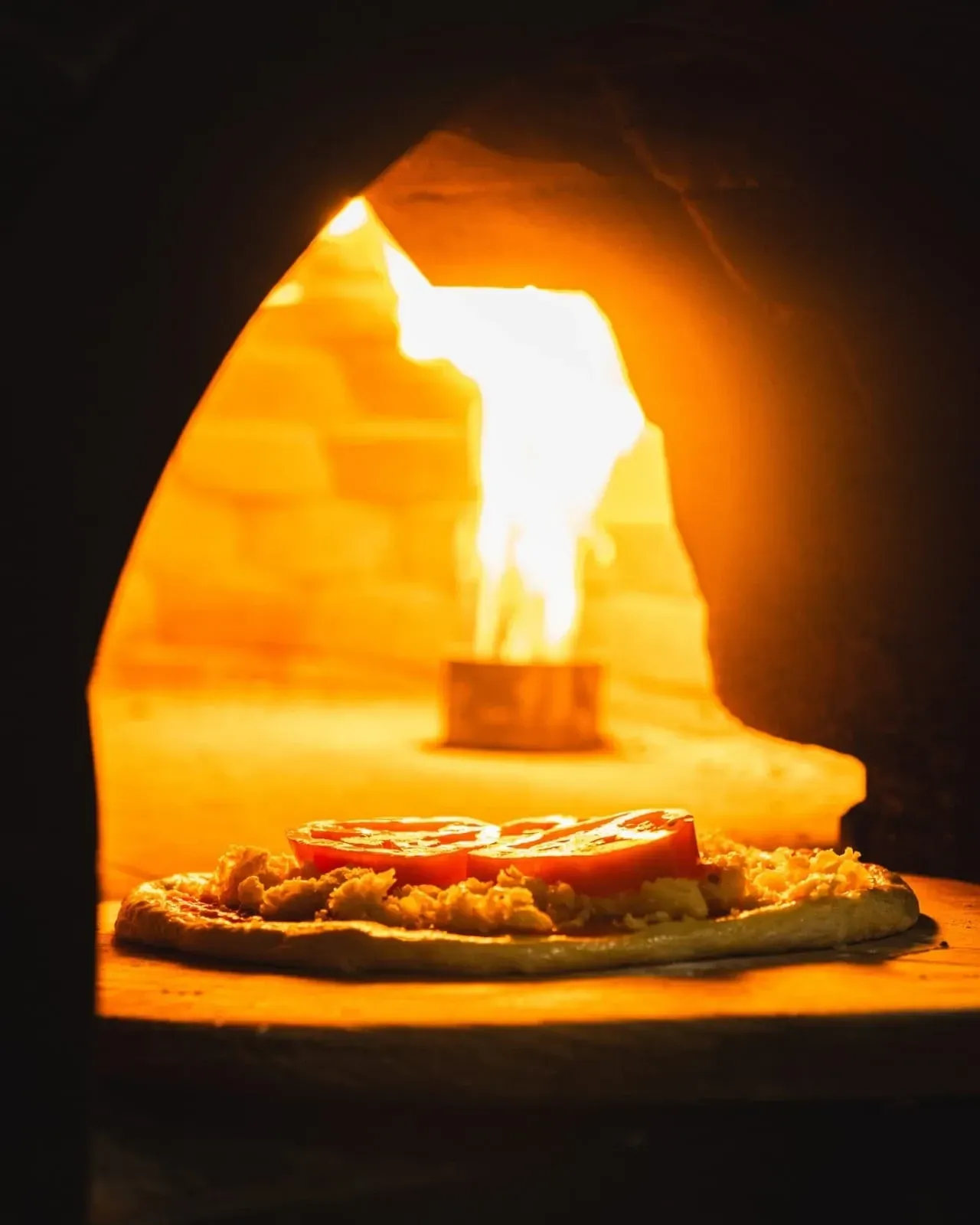 Pizza assando em forno a lenha com chamas brilhantes e um brilho alaranjado.