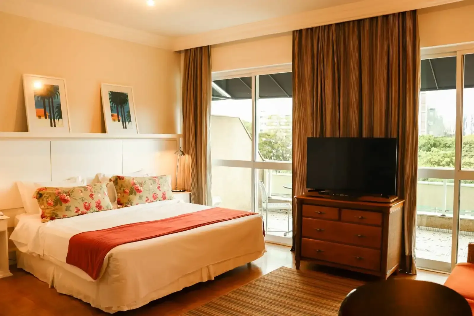 Quarto de hotel com cama, TV, varanda e cortinas marrons.