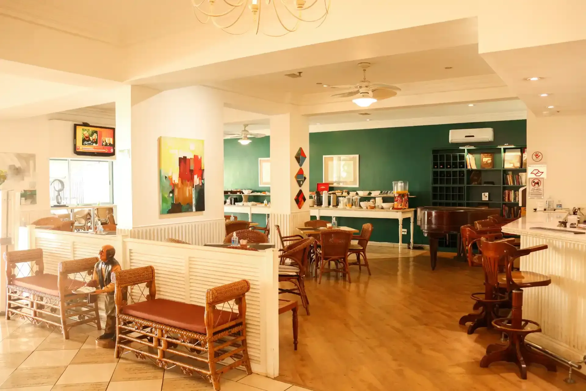 Café luminoso e arejado com mesas e cadeiras de madeira, paredes verde-azuladas e alguns clientes sentados no interior.