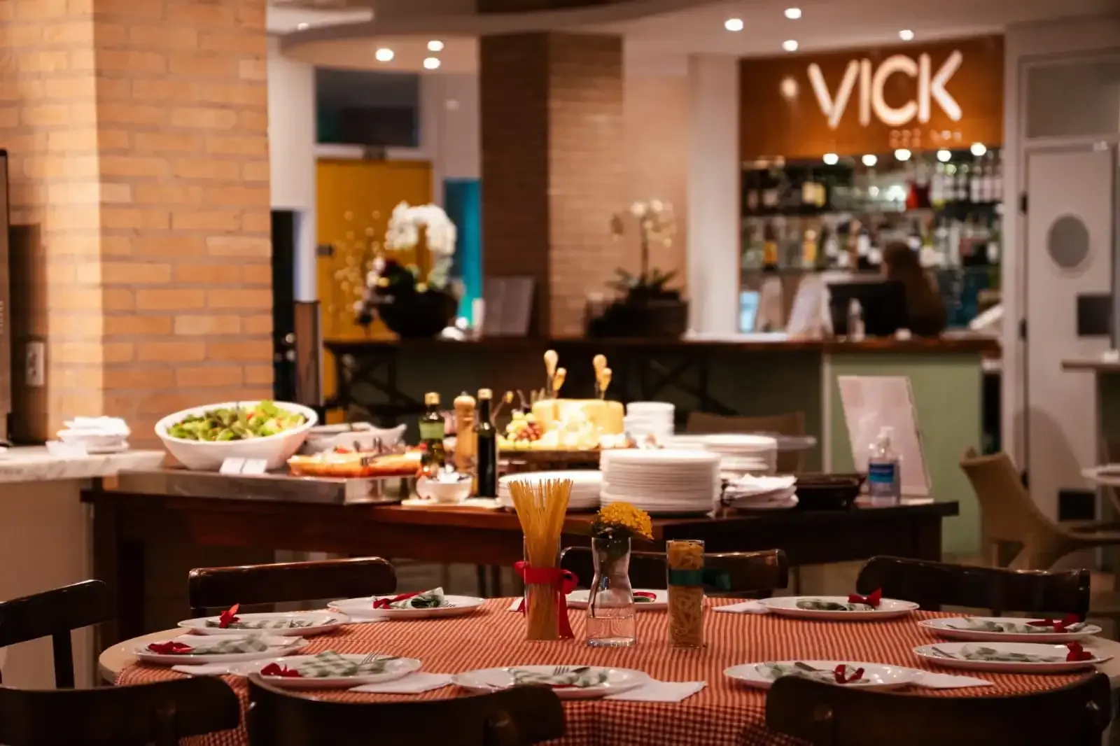 Interior de restaurante com mesa de buffet e mesa de jantar posta. Placa