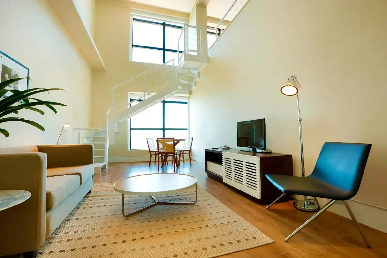 Sala de estar moderna em estilo loft com escada em espiral branca, mobília e janelas amplas.