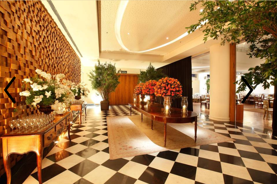 Hall de entrada elegante do hotel com piso xadrez preto e branco, arranjos florais e iluminação aconchegante.
