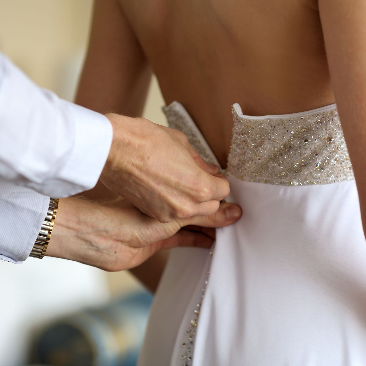 Mãos ajustando a parte de trás de um vestido branco bordado com miçangas e corpete de renda.