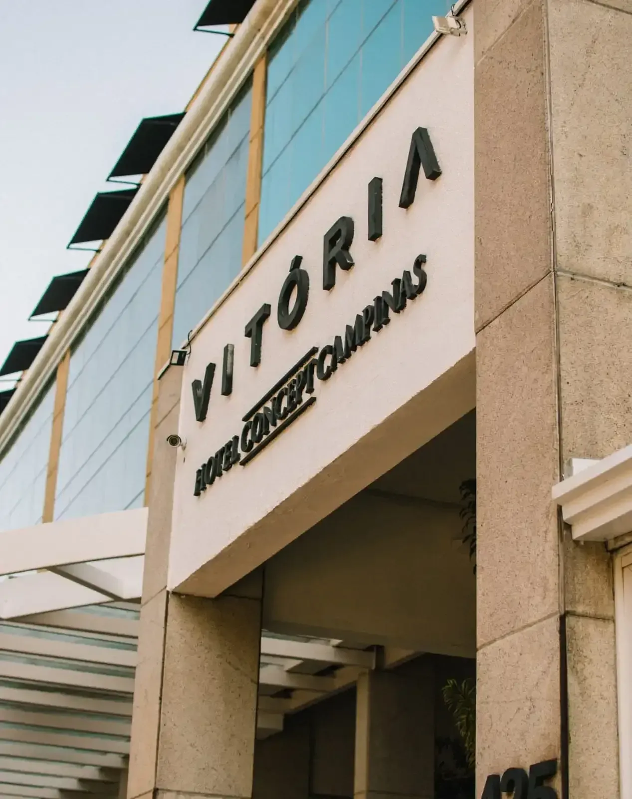 Entrada do Hotel Vitória Concept Campinas com placa, janelas de vidro e fachada bege.