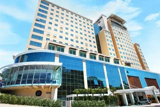 Moderno edifício de escritórios e hotel com fachada de vidro azul e alta torre bege sob um céu claro.
