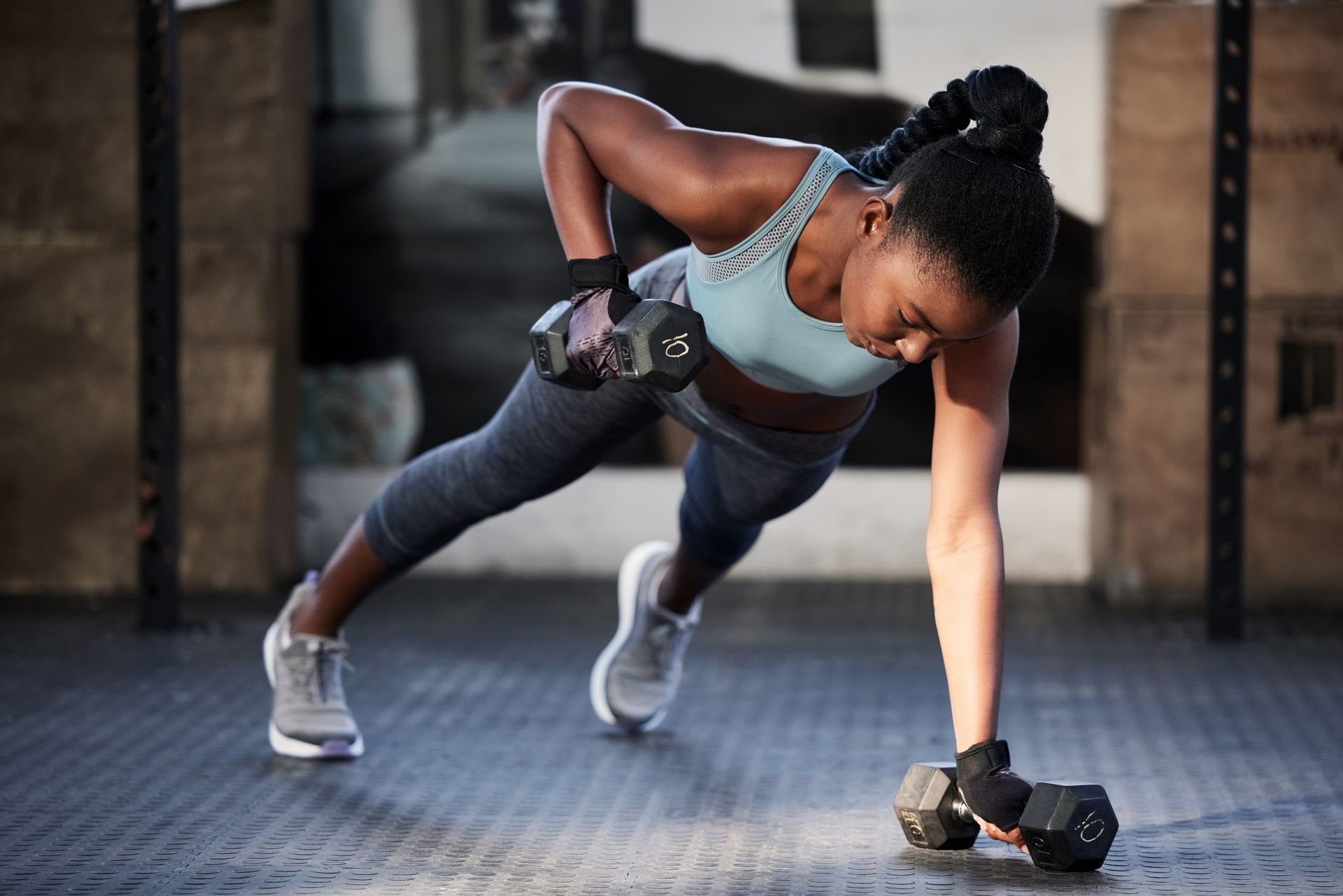 Woman doing a one-arm dumbbell push-up in a gym, wearing gray workout clothes.